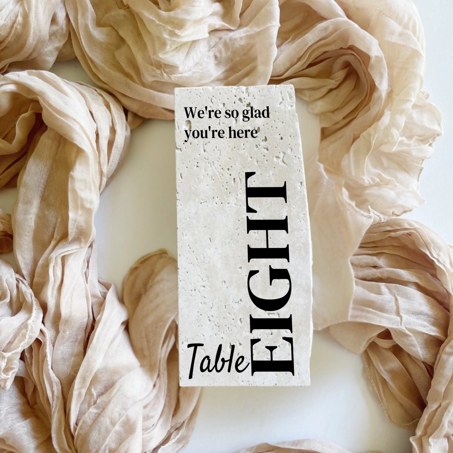 Travertine stone table number eight in portrait style, styled with neutral fabric for a wedding reception.